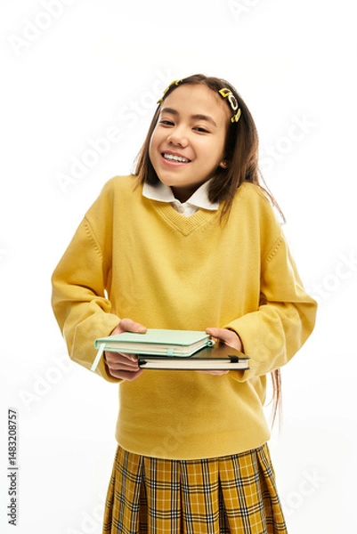 Fototapeta Stylish schoolgirl poses happily in a vibrant studio setting with books in hand