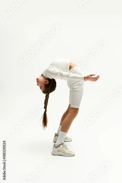 Fototapeta A girl showcases her flexibility in a trendy outfit while posing creatively in a studio