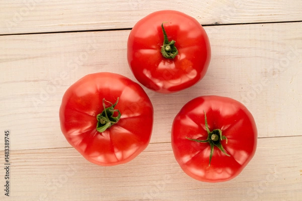 Fototapeta Three pink tomatoes  on a wooden table, close-up, top view.