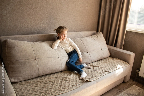 Fototapeta Young girl sitting on cozy sofa wearing casual clothing, with soft textures and warm lighting creating comfortable home atmosphere
