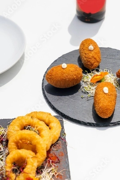 Obraz Spanish croquettes and fried calamari rings served on slate plates.