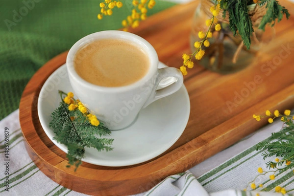 Fototapeta A cup of freshly brewed coffee on a wooden tray, decorated with yellow mimosa flowers, creating a bright and cozy spring mood.