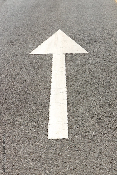 Fototapeta Directional arrow painted on asphalt road surface, guiding travelers forward, symbolizing journey and exploration during summer holidays