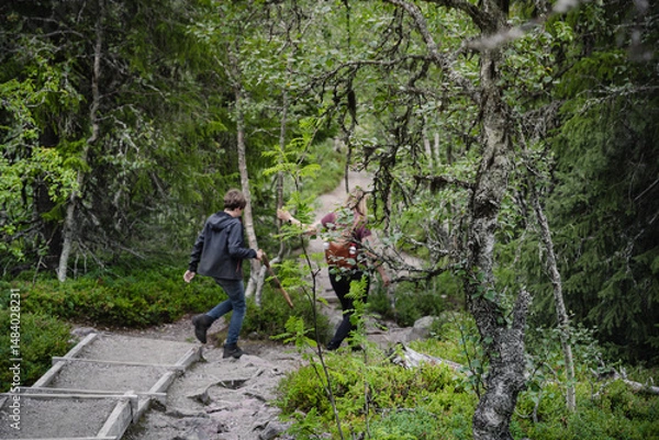 Fototapeta In beautiful Fulufjället National Park in Dalarna Sweden, a mother and her son hike along a winding path, enjoying the summer scenery surrounded by lush green trees and nature, walking out of focus