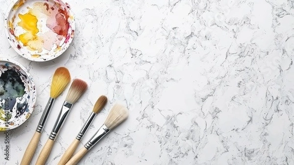 Fototapeta Artistic workspace scene of paintbrushes and watercolor palette resting on a marble tabletop surface overhead view