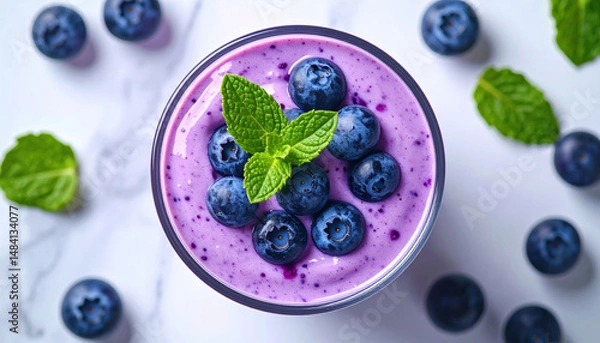 Fototapeta Creamy blueberry smoothie topped with fresh blueberries and mint leaves on marble surface.