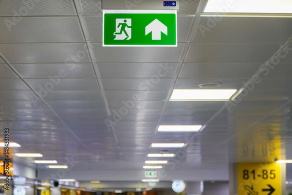 Obraz Green emergency exit sign on the ceiling of the airport,also ideal for airport safety practices
