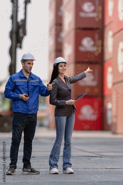 Fototapeta Industrial engineer standing at shipping container yard inspecting cargo delivering loading as plan. Woman manager and diverse ethnic worker checking import export container at logistic terminal dock.