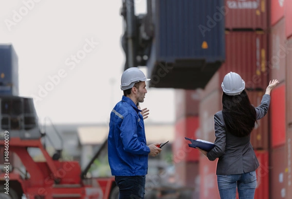 Fototapeta Industrial engineer standing at shipping container yard inspecting cargo delivering loading as plan. Woman manager and diverse ethnic worker checking import export container at logistic terminal dock.