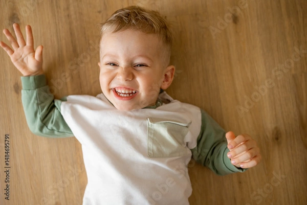 Fototapeta Happy child laughing playfully while lying on a wooden floor surface