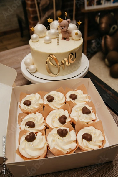 Obraz decorated cake with the inscription number one in gold letters for a children's birthday celebration and cupcakes in a kraft box lying next to it on the table, a delicious treat for guests