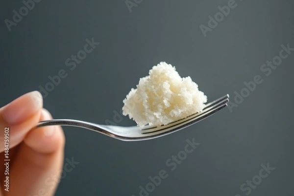 Fototapeta Close up of hand holding fork with pile of white food against a gray background in soft light