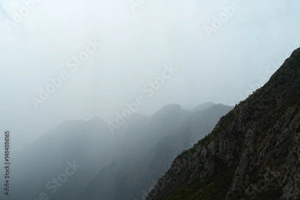 Fototapeta Fog covers mountain peaks on cloudy day