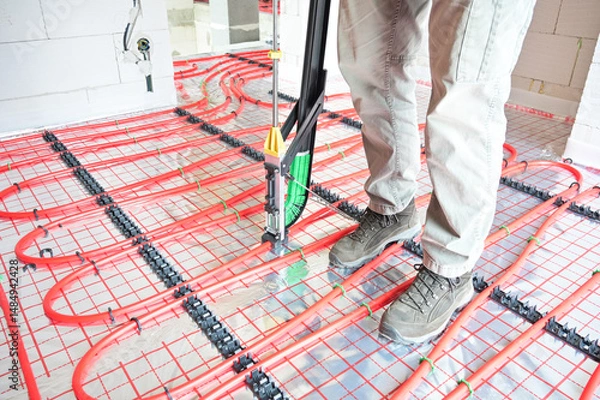 Fototapeta A technician skillfully installs an underfloor heating system using advanced technology, showcasing precise placement and modern plumbing techniques in a construction setting