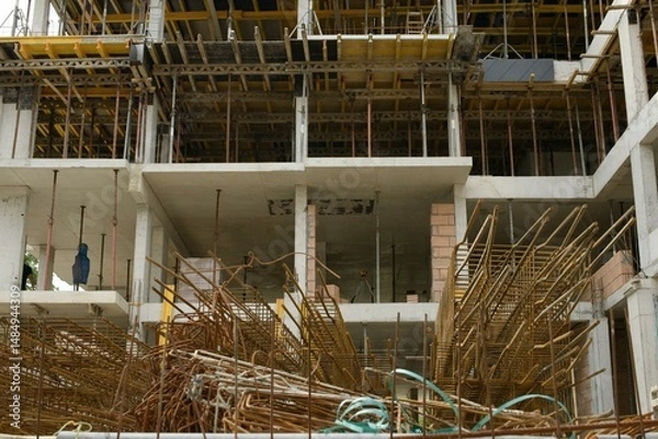 Fototapeta A reinforced concrete building frame at a construction site shows stacked rebar cages, formwork slabs, and scaffolding awaiting the next concrete pour