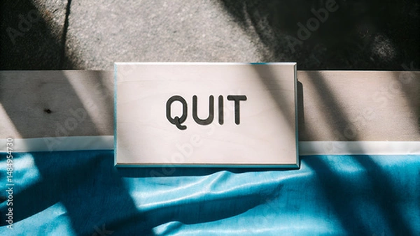 Fototapeta Quiet Quitting Job Burnout Employee A sign reading "QUIT" placed on a textured surface with shadows and vibrant colors.