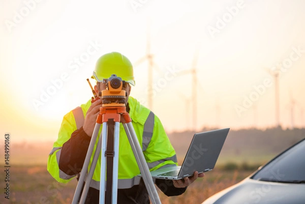 Fototapeta Engineer wearing uniform inspection and survey work in wind turbine farms rotation to generate electricity energy. Maintenance engineer working in wind turbine farm at sunset.