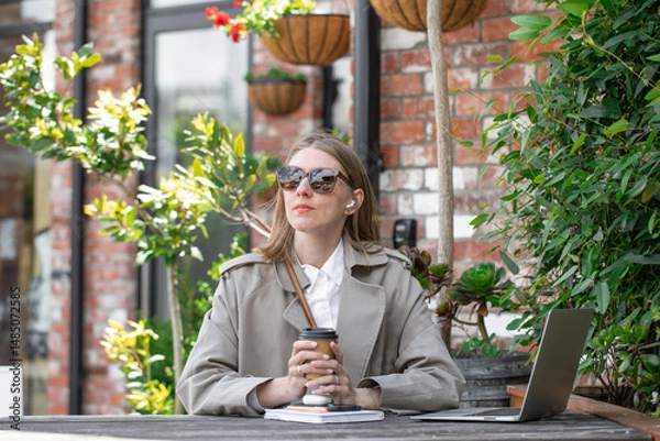 Obraz Businesswoman holding disposable cup of coffee at table in cafe. Remote work, freelancer