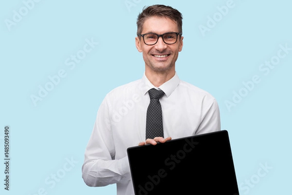 Fototapeta Professional-looking man in business attire confidently smiling and presenting a black screen laptop to the viewer, positioned against a clean and simple light blue backdrop.