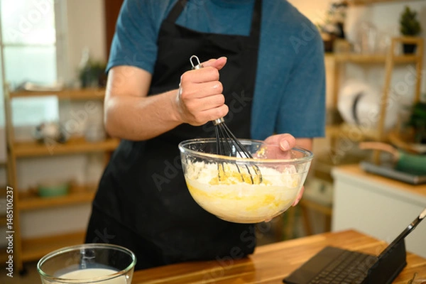 Fototapeta Man whisking pancake batter in a glass bowl while following recipe on digital tablet