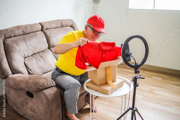 Obraz Portrait Of Elderly Male Review Product With Unboxing Package Showing Red Clothes While Doing Vlog