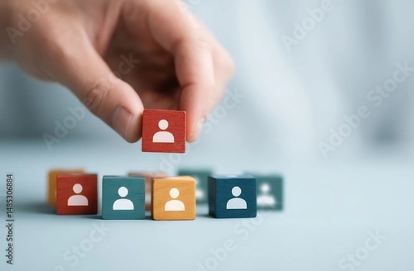 Fototapeta Hand placing a wooden block representing a person onto a group of similar blocks symbolizing teamwork, recruitment, or human resources management.