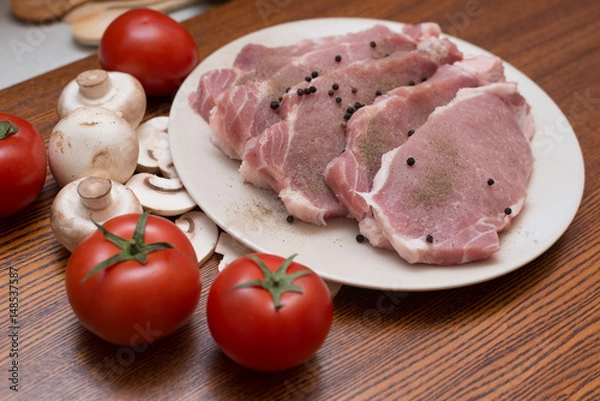 Fototapeta Slices of raw meat lie on a plate next to tomatoes and champignons