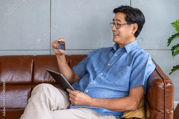 Fototapeta Asian senior man using tablet for online shopping with credit card at home
