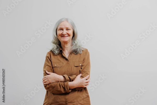 Fototapeta Smiling elderly woman with gray hair standing against a plain background in a casual outfit and relaxed pose during daylight