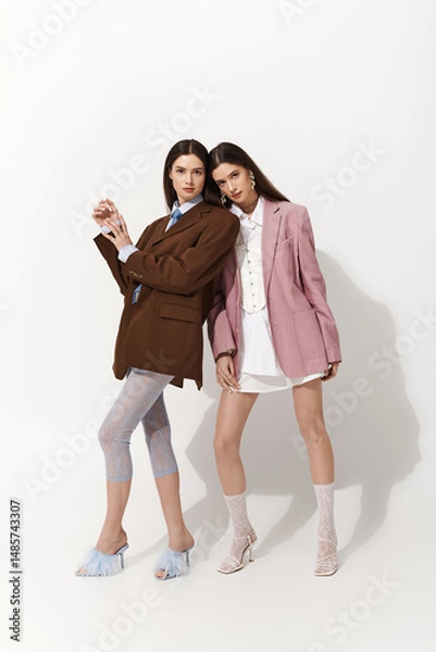 Fototapeta Stylish twin sisters showcasing unique fashion in a minimalistic studio setting