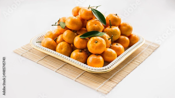 Fototapeta Mandarin oranges arranged in a white square container on top of sushi rolls on a white table