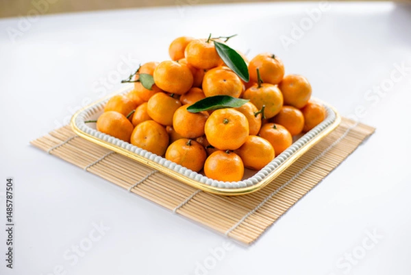 Fototapeta Mandarin oranges arranged in a white square container on top of sushi rolls on a white table