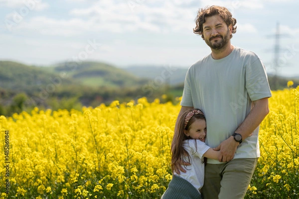 Obraz Father and daughter hugging in front of blooming yellow rapeseed field. Family emotions and leisure concept