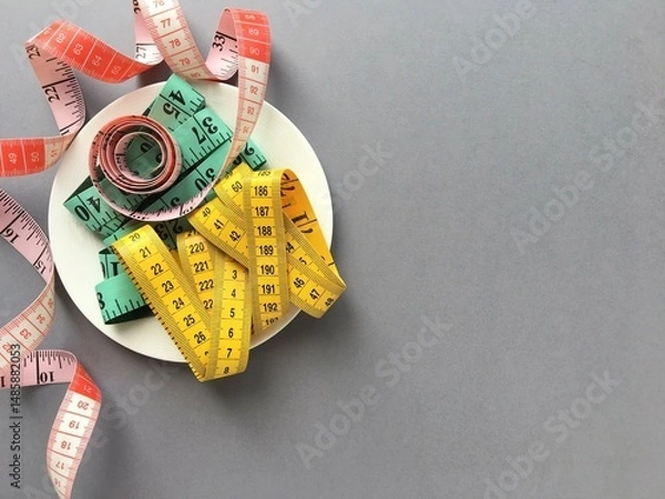 Obraz White plate with three colored measuring tapes on grey background