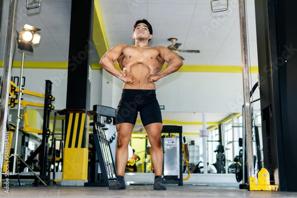 Obraz Young bodybuilder showing his muscles in a gym