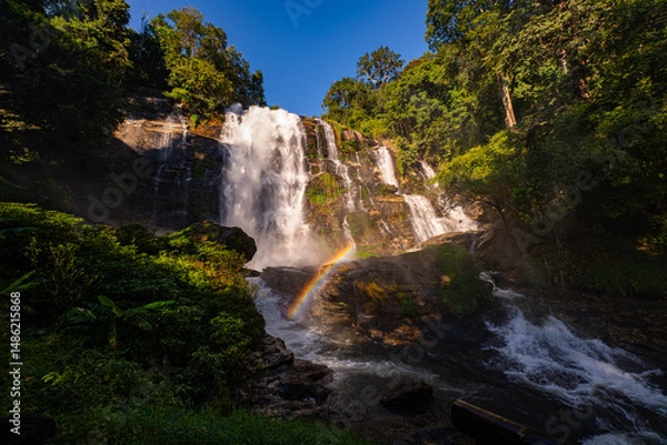 Obraz Wachirathan waterfall Chiang Mai is surrounded by lush greenery, with a vibrant rainbow forming in the mist. Water droplets hit by sunlight create rainbows that we can see all day long..