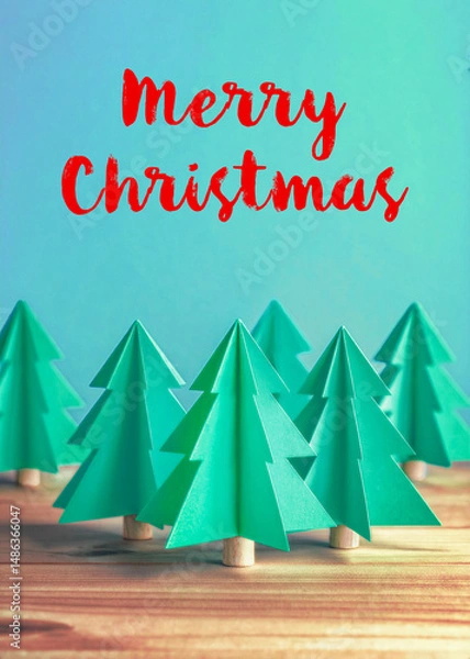 Fototapeta Trendy folded paper Christmas tree decorations on a wooden table against a turquoise green background that says Merry Christmas, easily replaced with your own personal message.