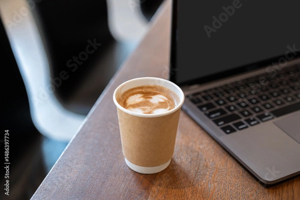 Fototapeta Close-up of Hot coffee latte with latte art milk foam in cup made of paper and laptop computer on wood desk office desk in coffee shop at the cafe,during business work concept