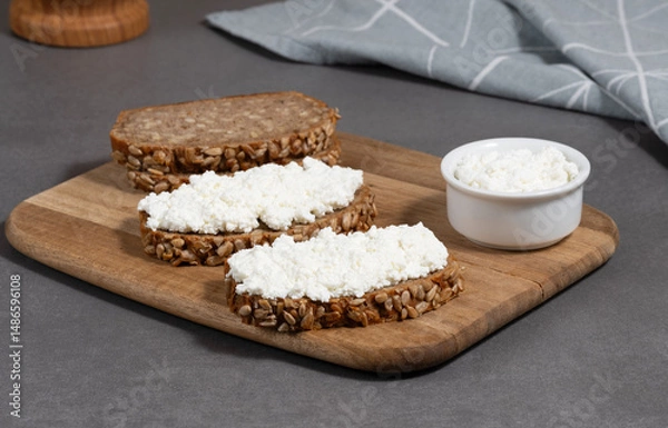 Fototapeta Delicious rye bread topped with cottage cheese on a wooden board in a modern kitchen setting