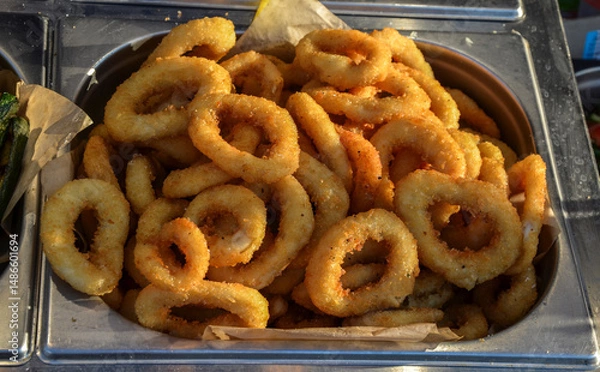 Fototapeta Golden fried calamari presented in stainless steel tray, showcasing their crispy texture and appeal. Perfect for seafood dining enthusiasts and culinary presentations in restaurants or buffet settings