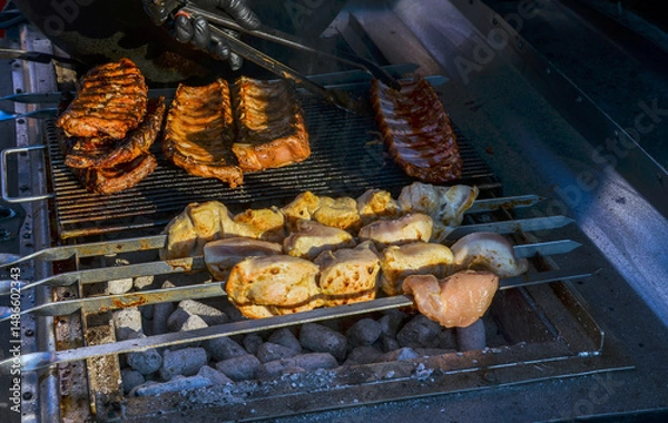 Fototapeta Grilled ribs and skewered meat cooking on a charcoal barbecue, showcasing outdoor grilling and culinary enjoyment
