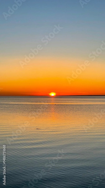 Fototapeta Beautiful sunset over the sea. The sun sets on the water. The sky is painted with bright colors. Summer evening. Sunset beach. Vertical photo.