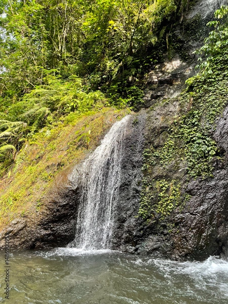 Fototapeta Waterfall in tropical rainforest flows over black rock cliffs