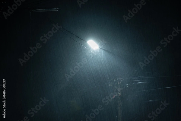 Fototapeta Falling raindrops on night background.Heavy rainy and wind with public street lights on black background.Rainy season and long exposure.