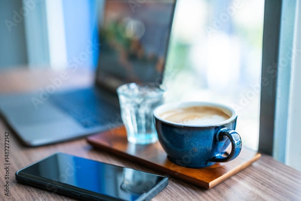 Obraz Close-up of Hot coffee latte with latte art milk foam in cup mug and laptop computer and smartphone on wood desk office desk in coffee shop at the cafe,during business work concept
