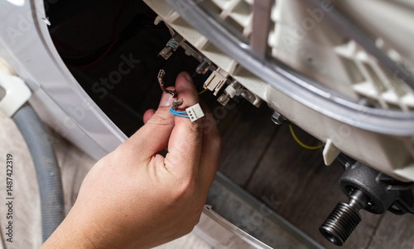Fototapeta The hand of the master removes the electrical chips to remove the heating element of the washing machine and the heating sensor. Repair of washing machines, industry