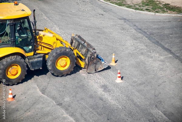 Fototapeta Modern yellow forklift stands on the road near the dug up road. Concept of emergency service for elimination of accident in water supply and sewerage. Copy space for text