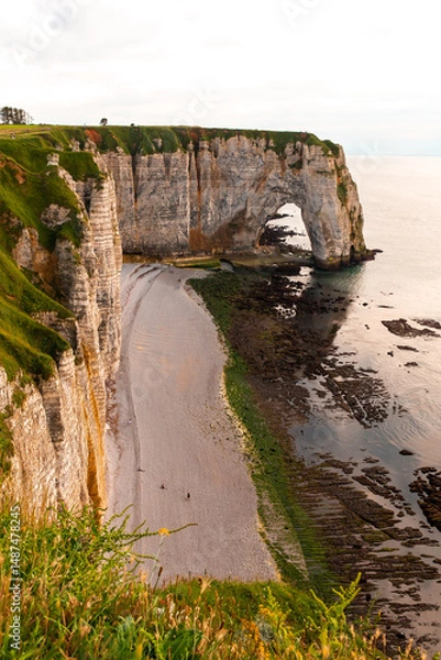 Fototapeta Stunning cliffs tower above the pebble beach in Etretat, France, where boats are anchored. The serene coastline reflects the beauty of nature at sunset.