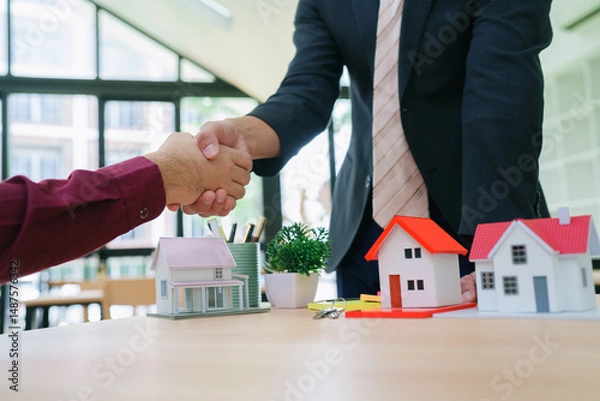 Obraz .Cheerful Asian real estate professional shaking hands with happy new homeowner, closing sale while holding documents and smiling. Couple shaking hands thanking real estate agent for successful apartm