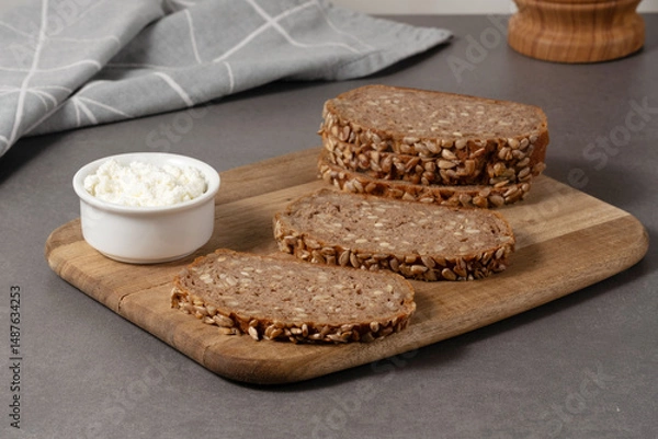 Fototapeta Delicious whole grain bread topped with creamy cottage cheese on a wooden board in a modern kitchen setting
